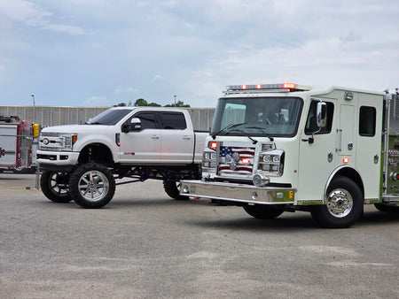 White fire engine parked beside a lifted Ford truck, shown as a vehicle reference